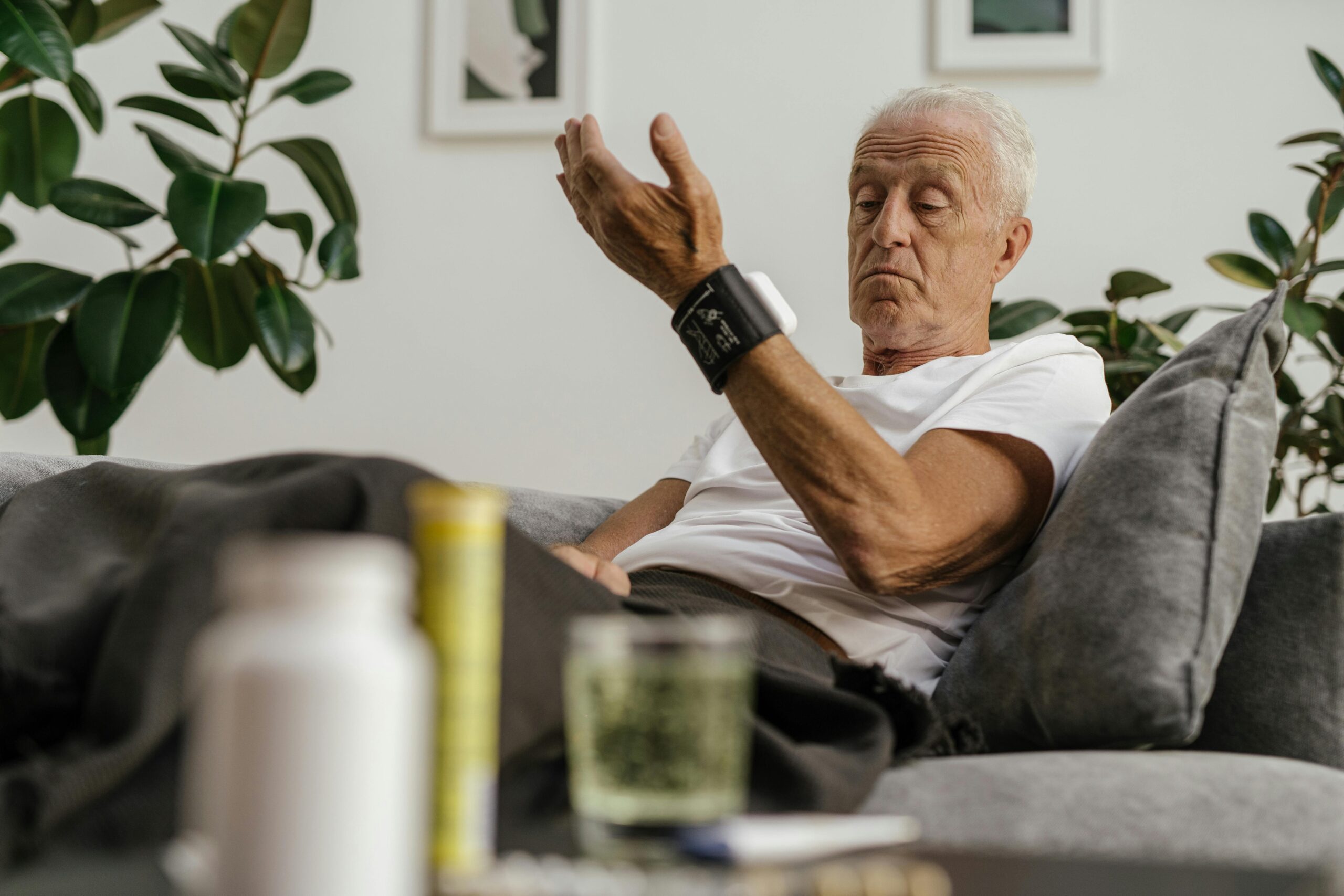 Elderly man checks his blood pressure using a wrist monitor in a comfortable living room setting.